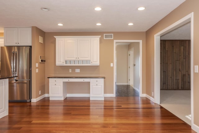 kitchen with dark wood-type flooring, high end fridge, white cabinets, and built in desk