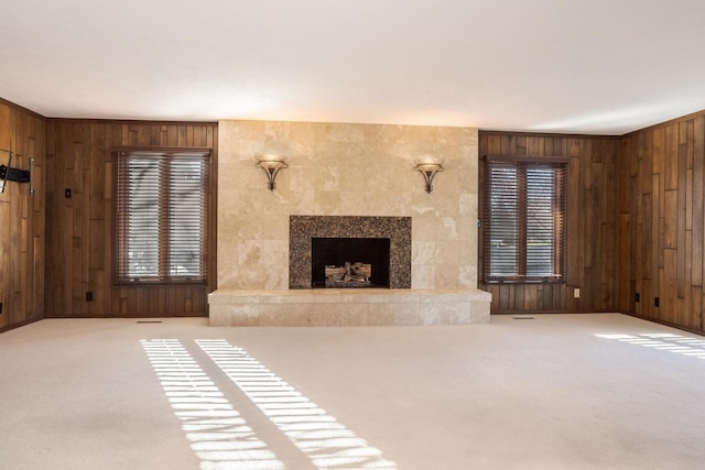 unfurnished living room with wood walls, light colored carpet, and a tiled fireplace