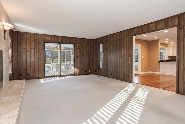 unfurnished living room featuring a ceiling fan, wood walls, and carpet floors