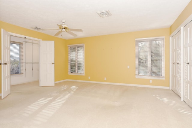 unfurnished bedroom featuring ceiling fan, light colored carpet, and two closets