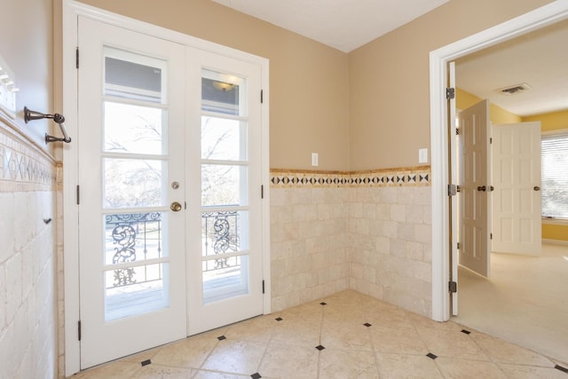 doorway with french doors, plenty of natural light, tile walls, and visible vents