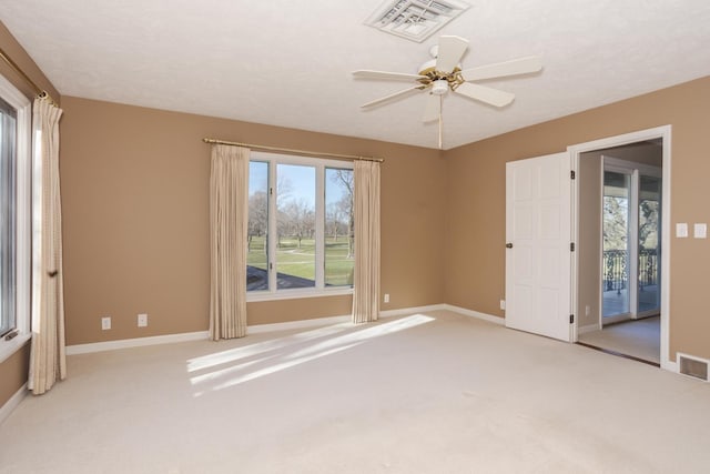 carpeted spare room with visible vents, baseboards, and a ceiling fan