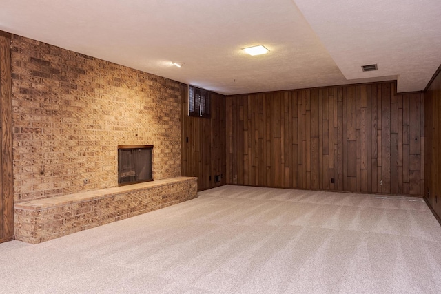 basement featuring carpet flooring, wood walls, a textured ceiling, and a brick fireplace