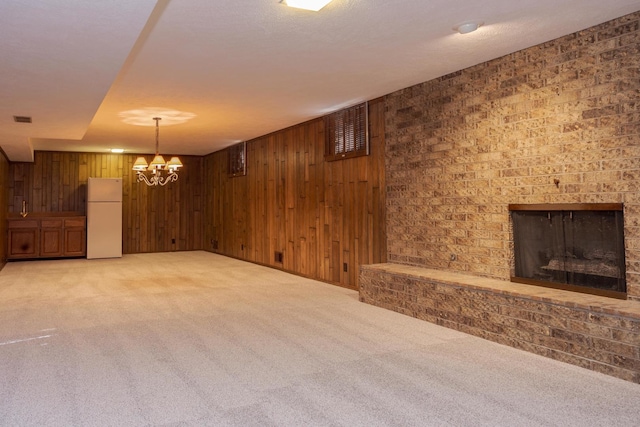 unfurnished living room featuring visible vents, wooden walls, an inviting chandelier, light colored carpet, and a brick fireplace