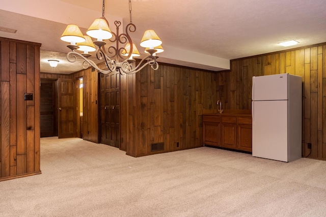 interior space with visible vents, a notable chandelier, freestanding refrigerator, wooden walls, and light colored carpet