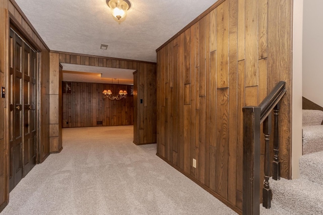 hallway with an inviting chandelier, carpet flooring, crown molding, and wood walls