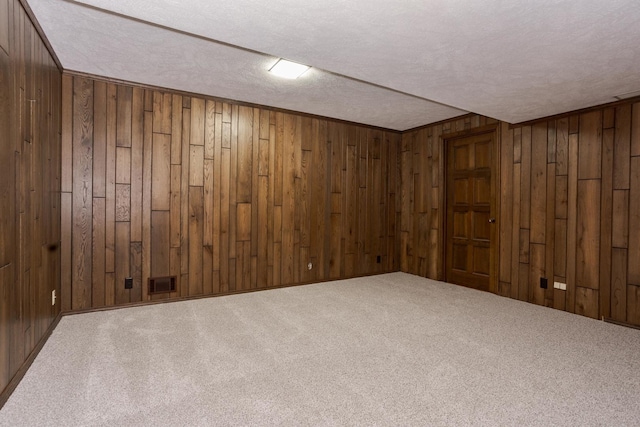 spare room with visible vents, carpet flooring, a textured ceiling, and wood walls