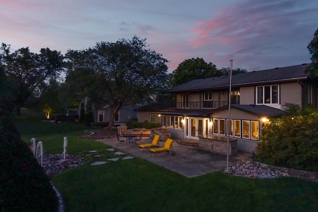 back of house at dusk with a lawn, french doors, and a patio