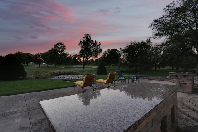 patio terrace at dusk featuring a lawn