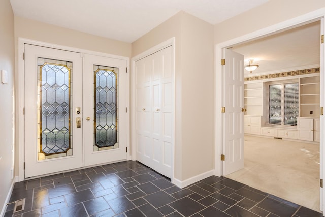 foyer featuring stone tile floors, dark carpet, french doors, and baseboards