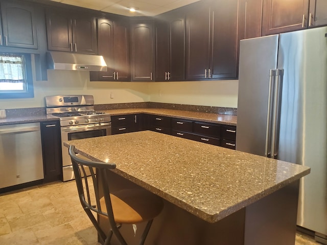 kitchen with stone countertops, light tile patterned floors, a kitchen breakfast bar, a kitchen island, and appliances with stainless steel finishes