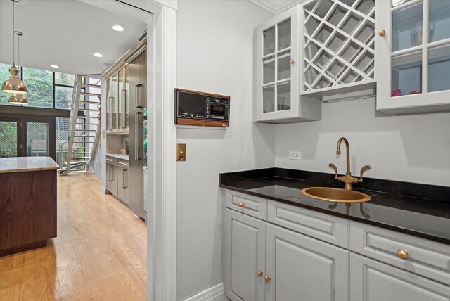 kitchen featuring dark stone counters, sink, light hardwood / wood-style flooring, and pendant lighting