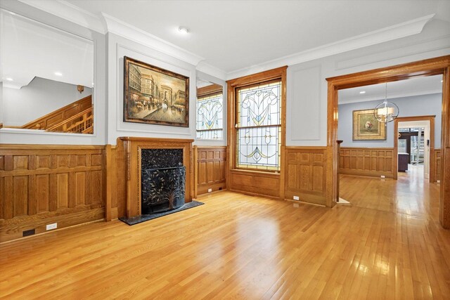 unfurnished living room featuring an inviting chandelier, light hardwood / wood-style flooring, a high end fireplace, and ornamental molding