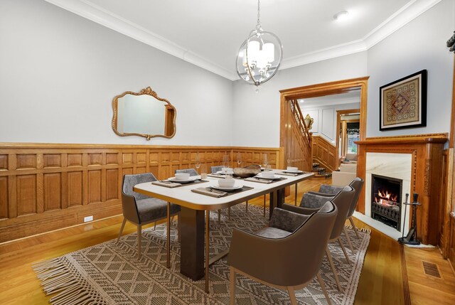 dining space with crown molding, an inviting chandelier, light wood-type flooring, and a premium fireplace