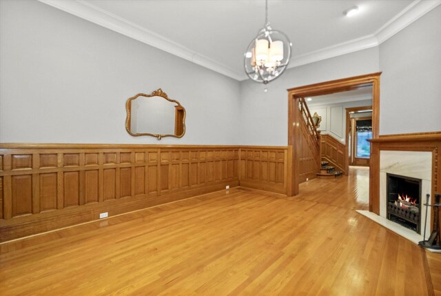 interior space featuring light hardwood / wood-style floors, an inviting chandelier, ornamental molding, and a high end fireplace