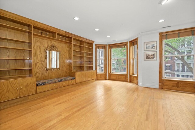 unfurnished living room with built in features, light wood-type flooring, and a healthy amount of sunlight