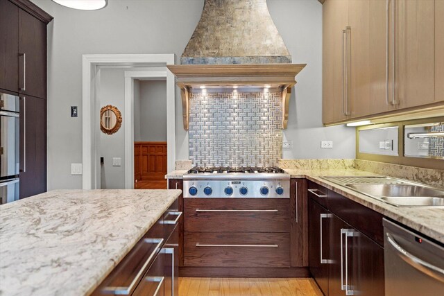 kitchen with light wood-type flooring, tasteful backsplash, dishwasher, light stone countertops, and gas stovetop