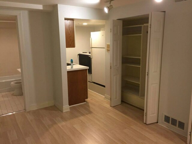 unfurnished bedroom with light wood-type flooring, white refrigerator, a closet, and ensuite bath