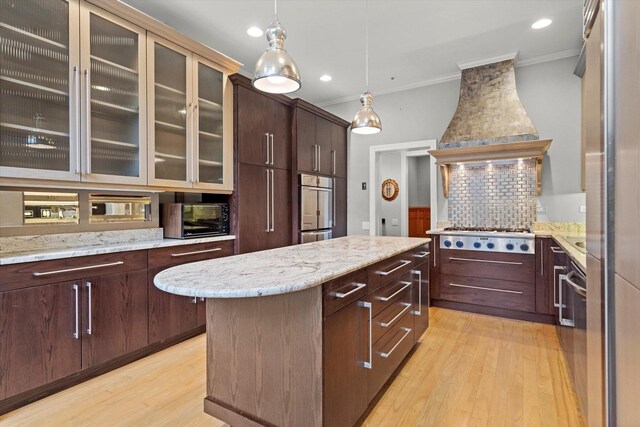 kitchen featuring backsplash, custom range hood, light hardwood / wood-style floors, a kitchen island, and stainless steel appliances