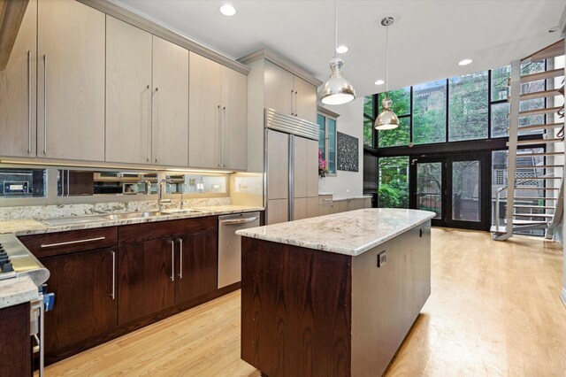 kitchen with light stone counters, light wood-type flooring, pendant lighting, paneled built in fridge, and a kitchen island