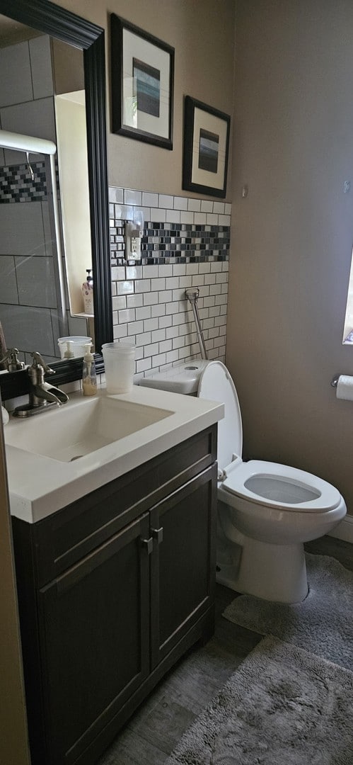 bathroom with toilet, a shower, wood-type flooring, decorative backsplash, and vanity