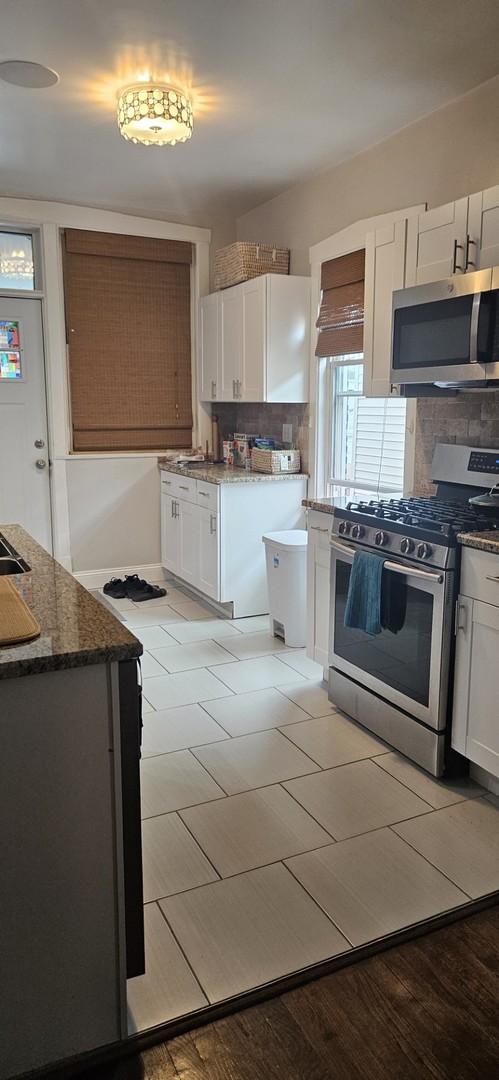 kitchen with light wood-type flooring, dark stone counters, white cabinetry, backsplash, and stainless steel appliances