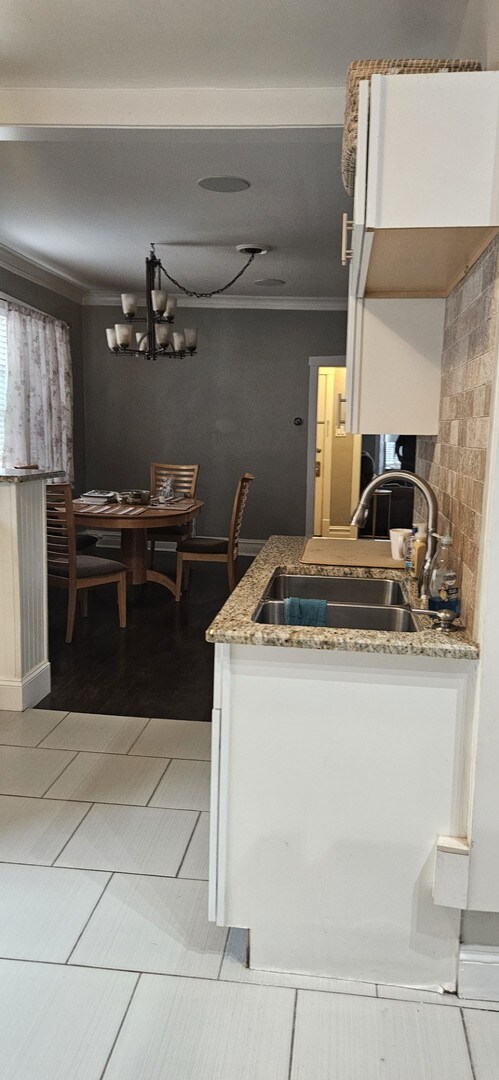 kitchen featuring an inviting chandelier, crown molding, light wood-type flooring, light stone counters, and sink