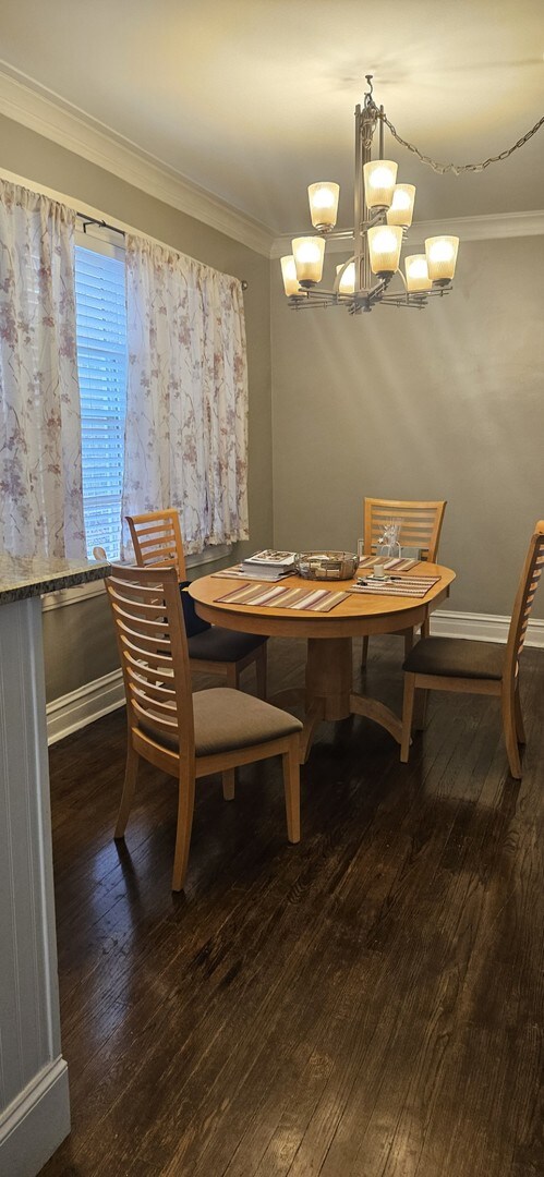 dining room featuring dark wood-type flooring, a notable chandelier, and ornamental molding