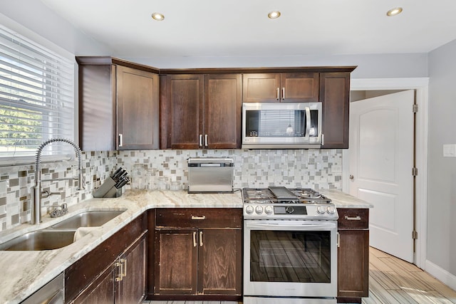 kitchen featuring backsplash, light wood-type flooring, light stone counters, stainless steel appliances, and sink