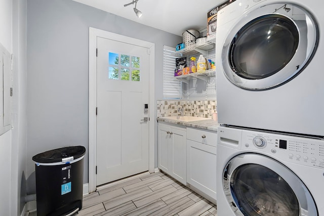 clothes washing area featuring stacked washer / dryer, cabinet space, a sink, and wood finish floors