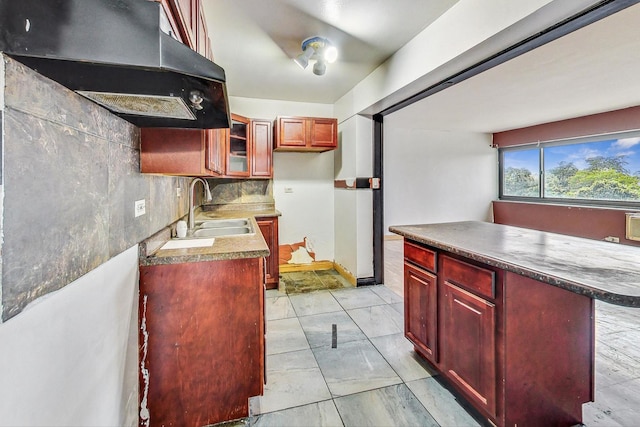 kitchen featuring reddish brown cabinets, range hood, a sink, a center island, and glass insert cabinets