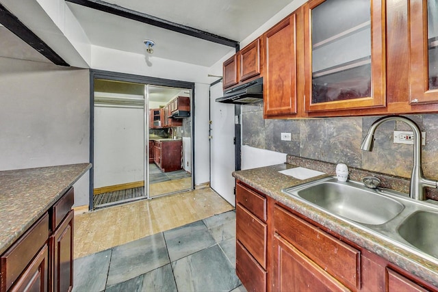 kitchen featuring dark countertops, a sink, tasteful backsplash, and glass insert cabinets