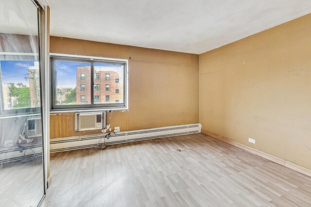 spare room featuring a wall mounted AC, baseboards, and wood finished floors