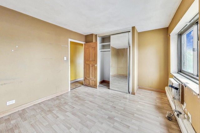 unfurnished bedroom featuring light wood finished floors, baseboards, and a closet