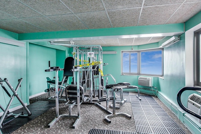 workout room featuring baseboards, a wall mounted air conditioner, and a paneled ceiling
