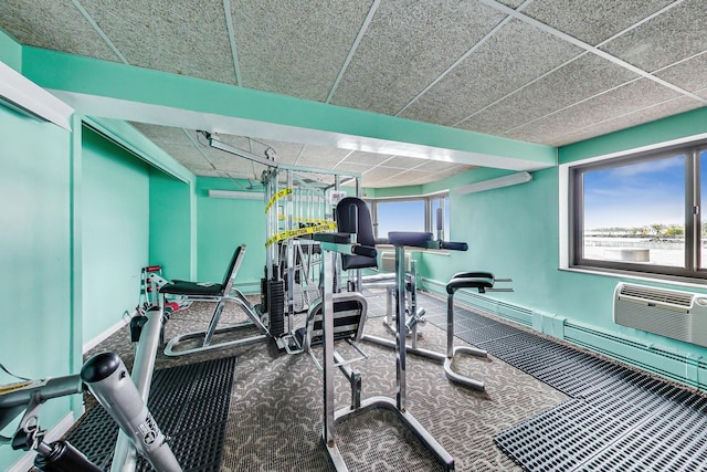 exercise room with carpet, baseboards, an AC wall unit, and a paneled ceiling