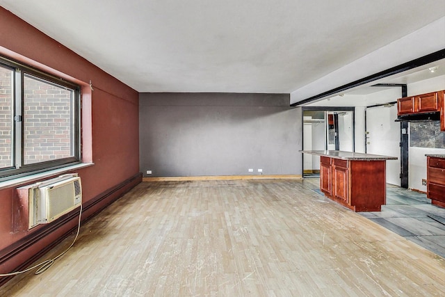 unfurnished living room with an AC wall unit, baseboards, and light wood finished floors