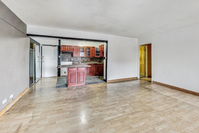 kitchen with decorative backsplash, baseboards, dark brown cabinets, a kitchen island, and glass insert cabinets
