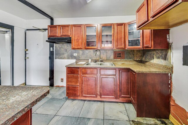kitchen with reddish brown cabinets, glass insert cabinets, a sink, and tasteful backsplash