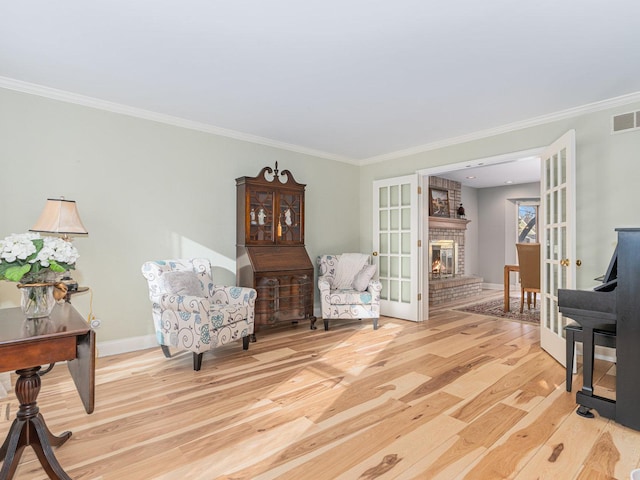 sitting room with french doors, crown molding, a brick fireplace, and light hardwood / wood-style flooring