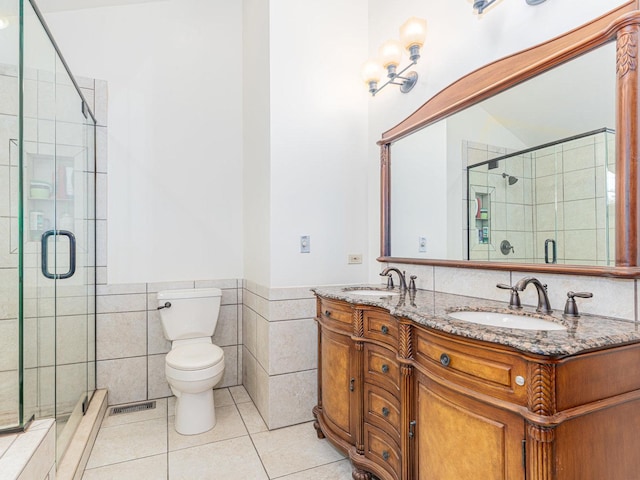 bathroom with a shower with door, tile walls, vanity, tile patterned floors, and toilet