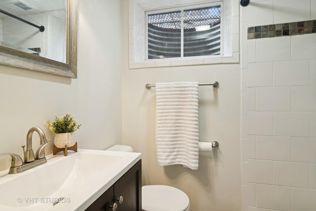 bathroom featuring toilet, vanity, and tiled shower