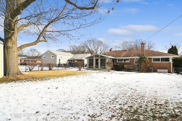 snow covered house featuring central AC unit and a sunroom