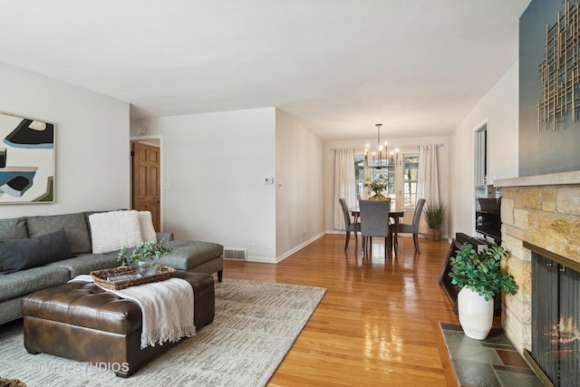 living room featuring a chandelier, wood-type flooring, and a stone fireplace