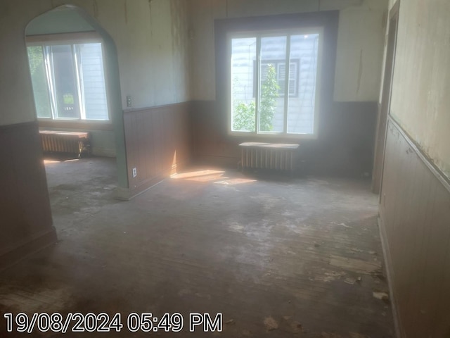 spare room featuring radiator, wainscoting, radiator heating unit, and unfinished concrete floors