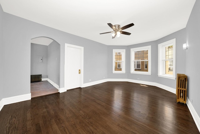 empty room with dark hardwood / wood-style floors, ceiling fan, and radiator heating unit