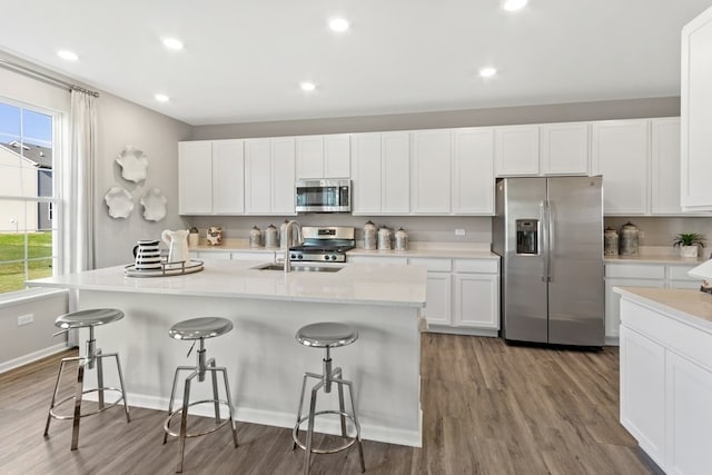 kitchen featuring hardwood / wood-style floors, appliances with stainless steel finishes, white cabinetry, and an island with sink