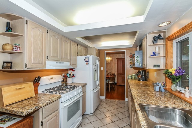 kitchen featuring light stone countertops, white appliances, light brown cabinetry, light tile patterned floors, and a raised ceiling