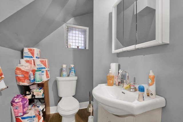 bathroom with toilet, wood finished floors, vanity, baseboards, and vaulted ceiling