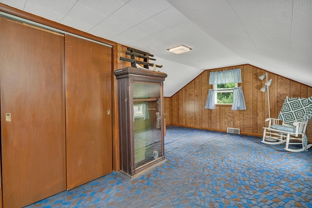 additional living space with vaulted ceiling, carpet, visible vents, and wooden walls